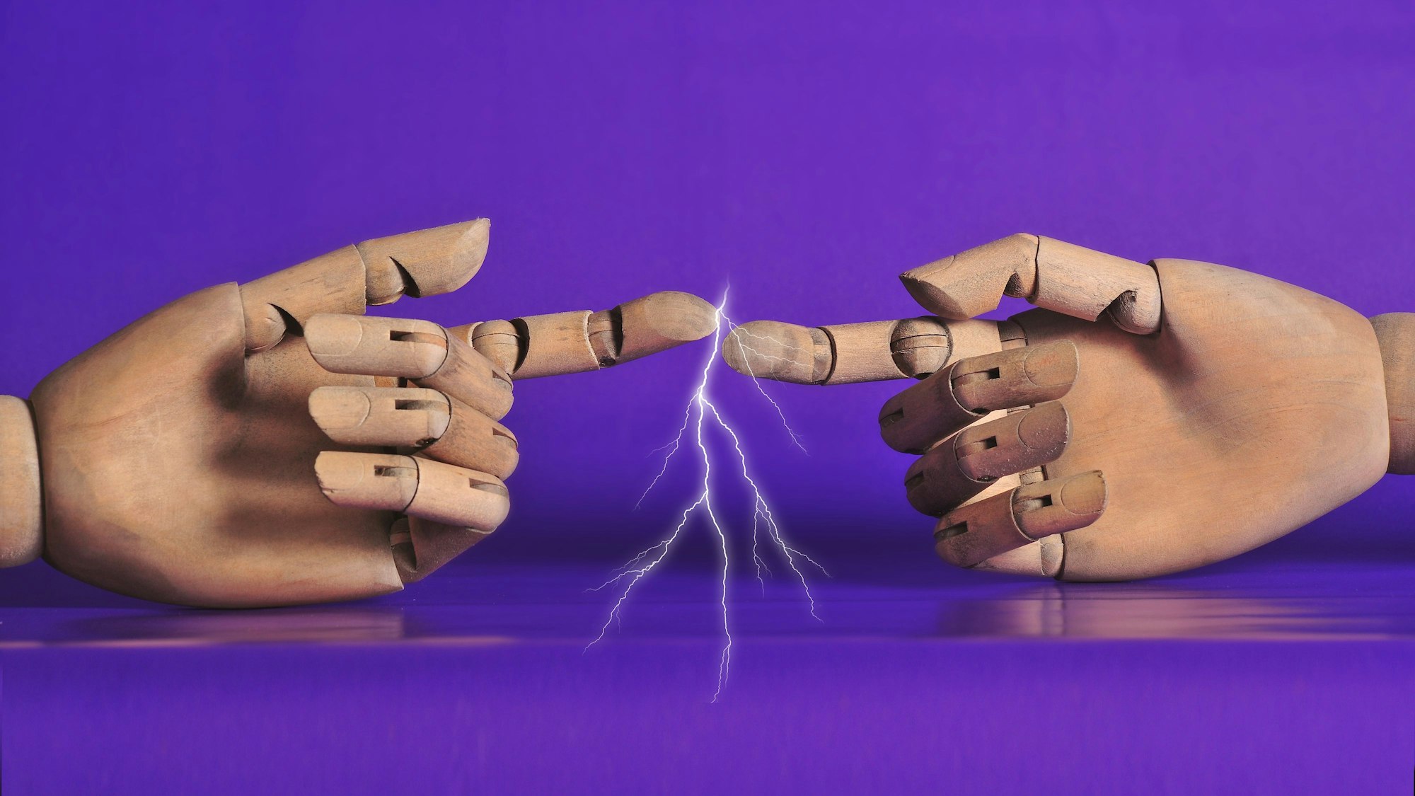 Zwischen zwei Händen aus Holz spannt sich ein Funken.
