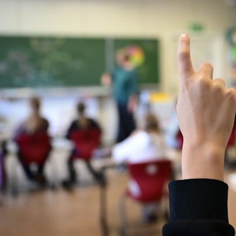 Kinder zeigen in einer Schulklasse auf.