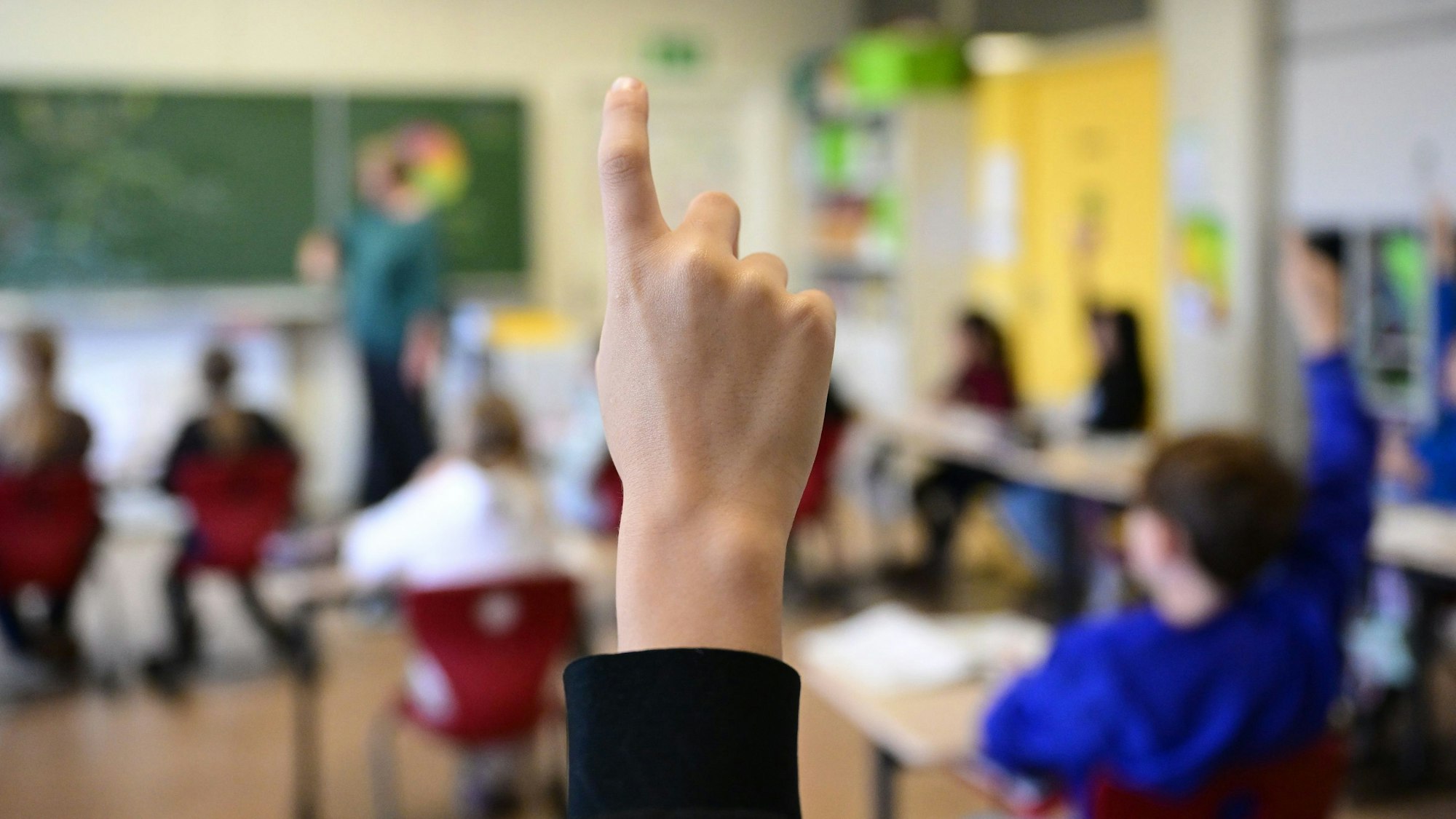 Kinder zeigen in einer Schulklasse auf.