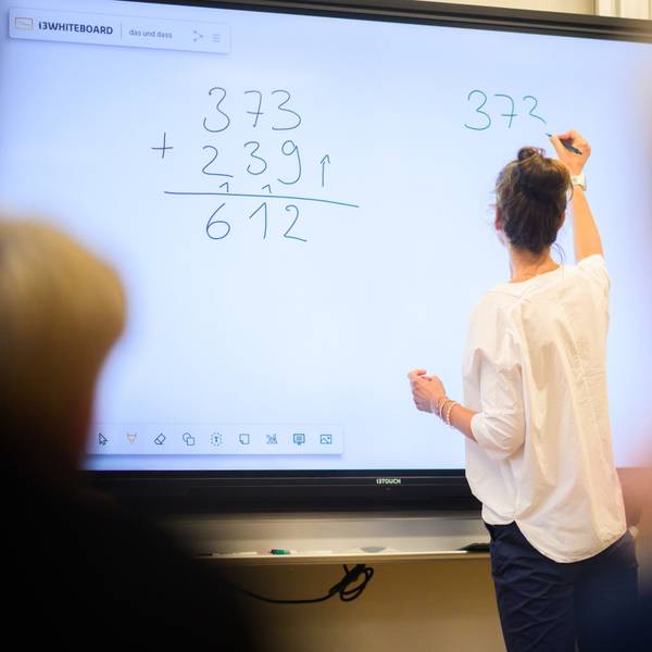 Eine Lehrerin schreibt eine Mathematikaufgabe auf eine digitale Schultafel im Klassenraum einer 4. Klasse einer Grundschule.