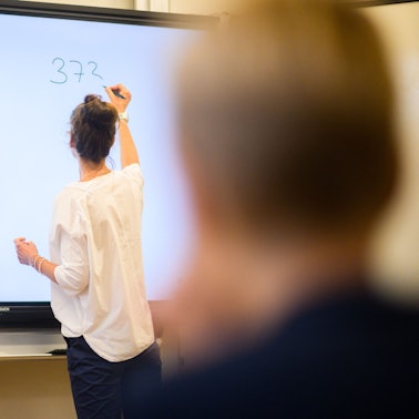 Eine Lehrerin schreibt eine Mathematikaufgabe auf eine digitale Schultafel im Klassenraum einer 4. Klasse einer Grundschule.