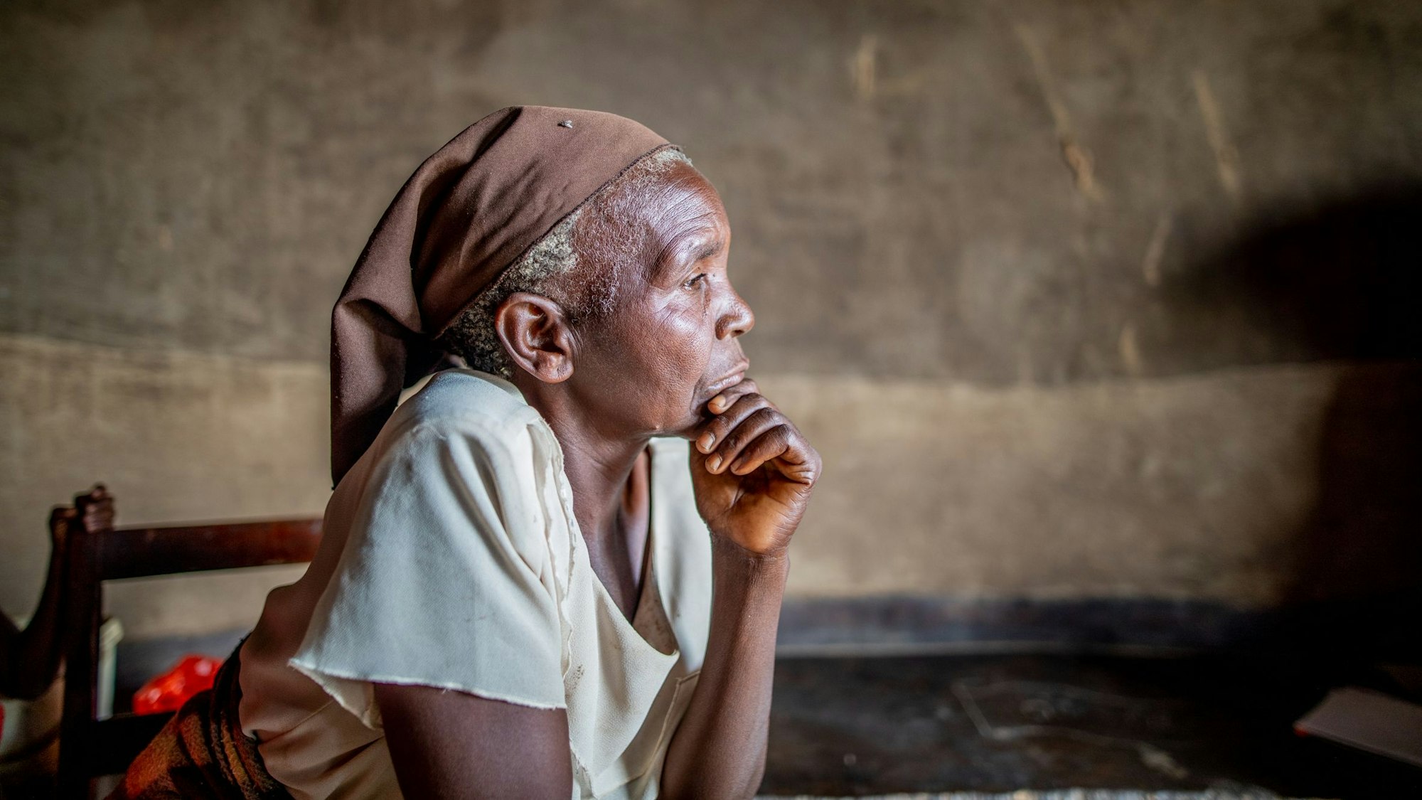 Auf dem Bild ist die sitzende 61-jährige Frau zu sehen, die das Kinn mit der Hand abstützt. Im Hintergrund eine braune Wand.