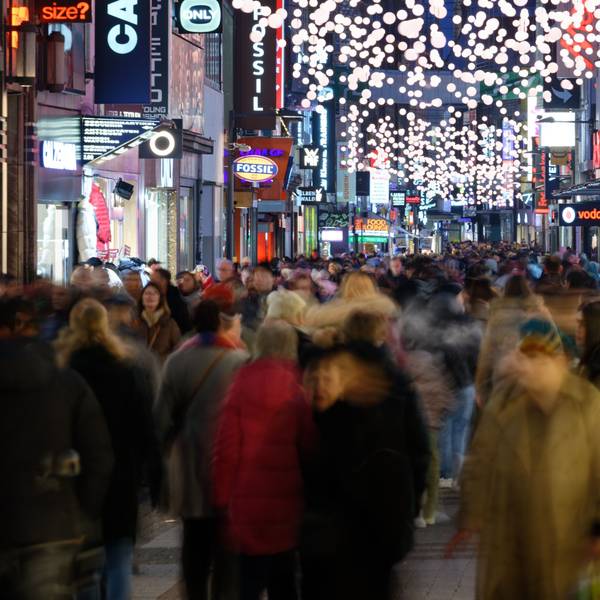 Einkäufer gehen durch eine mit Weihnachtslichtern geschmückte Einkaufsstraße