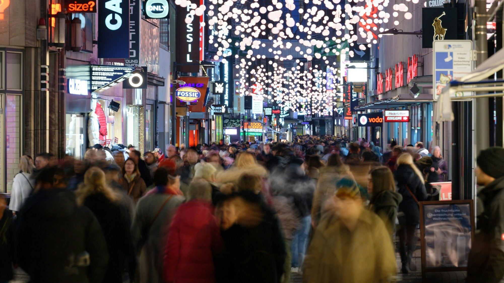 Einkäufer gehen durch eine mit Weihnachtslichtern geschmückte Einkaufsstraße