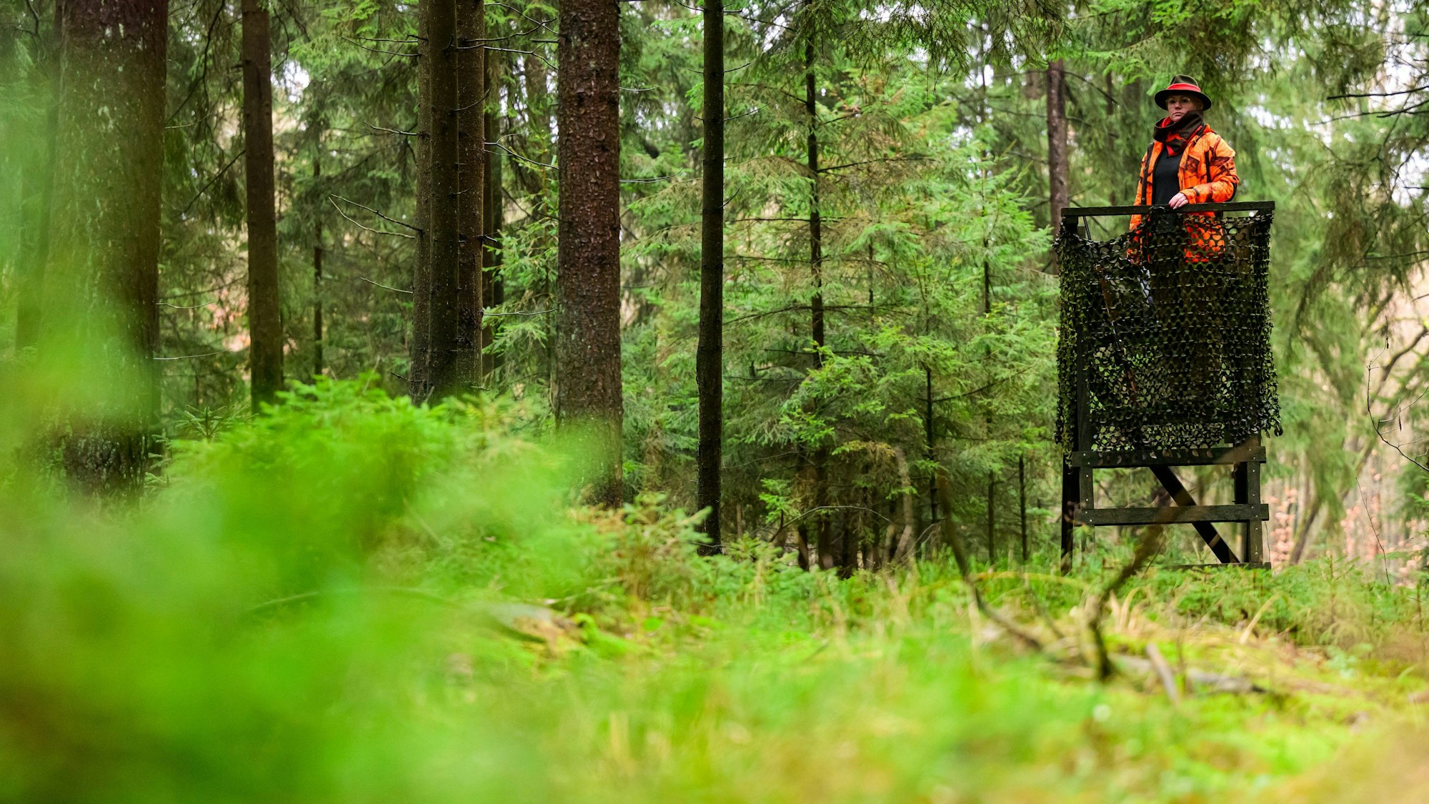 Eine Jägerin steht auf einem Hochsitz.