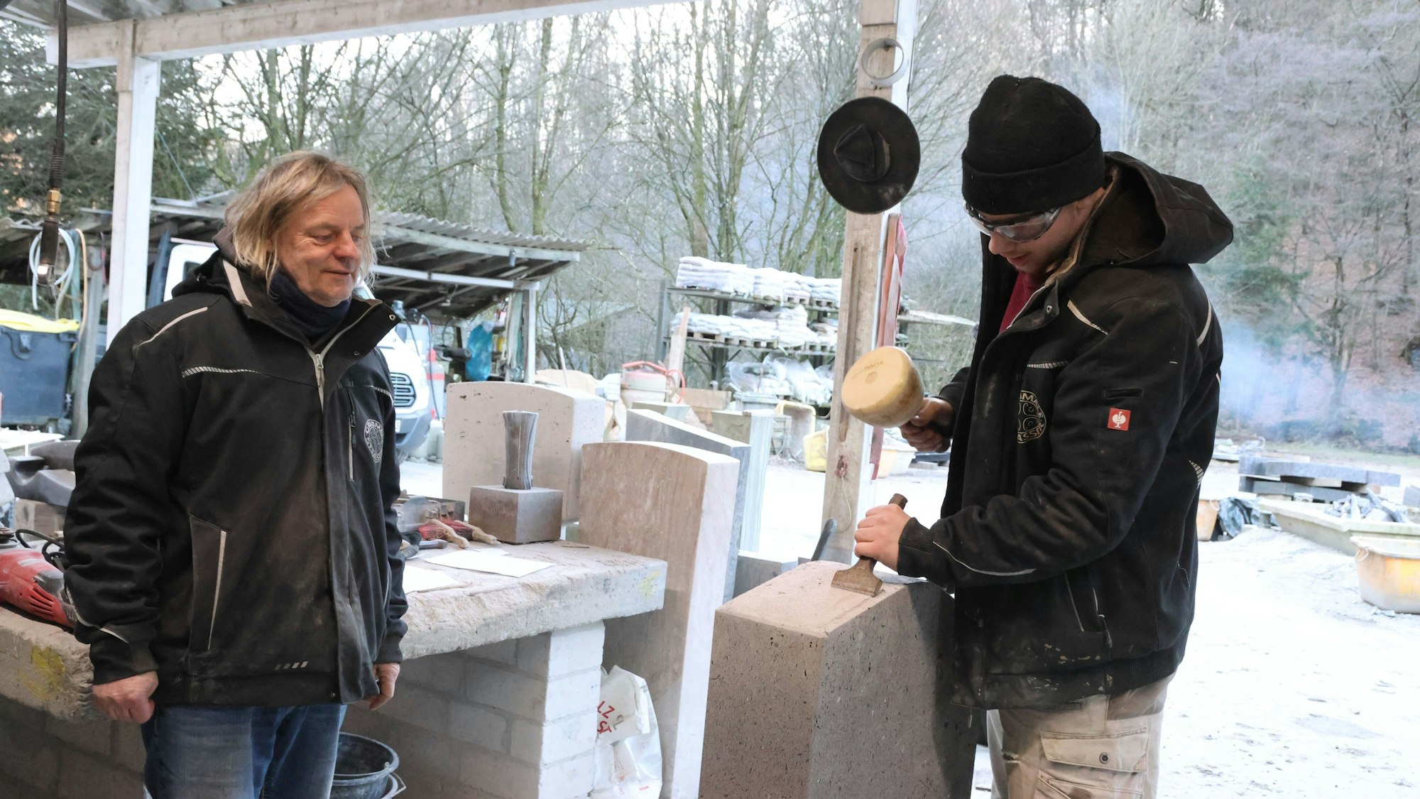 Steinmetz Thomas Sträßer beobachtet die Arbeit seines Neffen Jasper Sträßer, der einen Basaltstein bearbeitet.