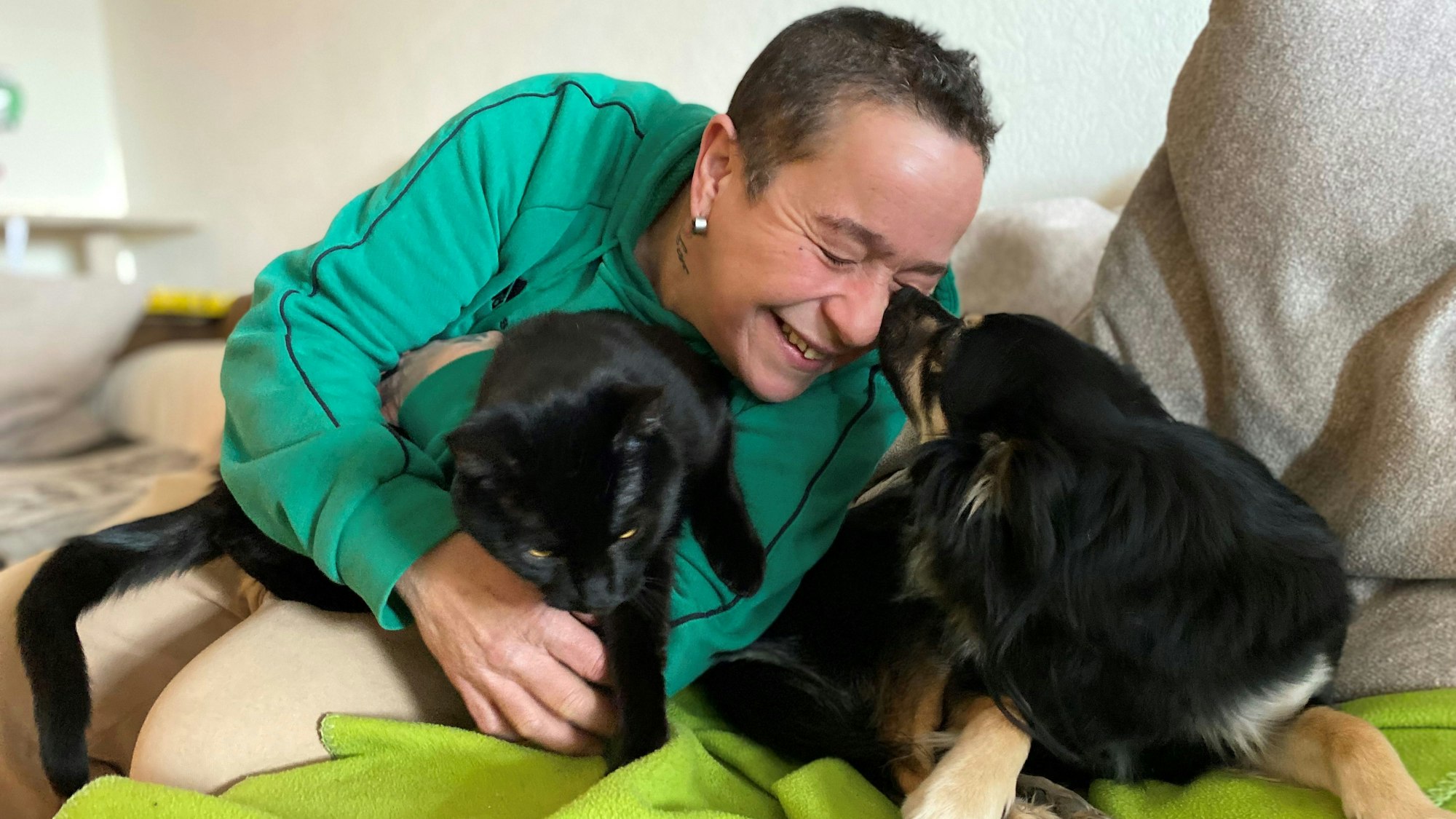 Tanja Liguori liegt mit einer schwarzen Katze und einem schwarzen Hund auf der Couch.