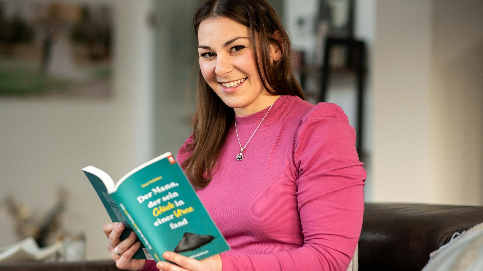 Das Bild zeigt Sara Schütze auf ihrer Couch. In den Händen hält sie ihren eigenen Roman.