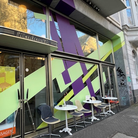 Die Front eines Cafés ist mit breiten lila und lindgrün-farbenen Streifen beklebt.