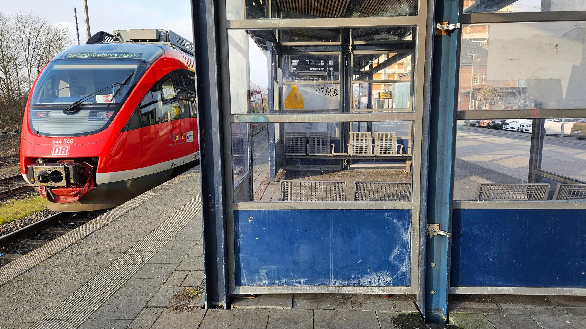 Ein Zug steht an einem Bahnsteig, im Wartehäuschen sind viele Scheiben zerschlagen.