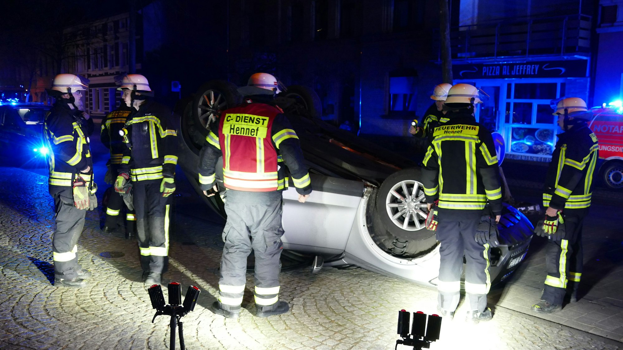 Feuerwehrleute stehen vor einem Auto, das auf dem Dach liegt.
