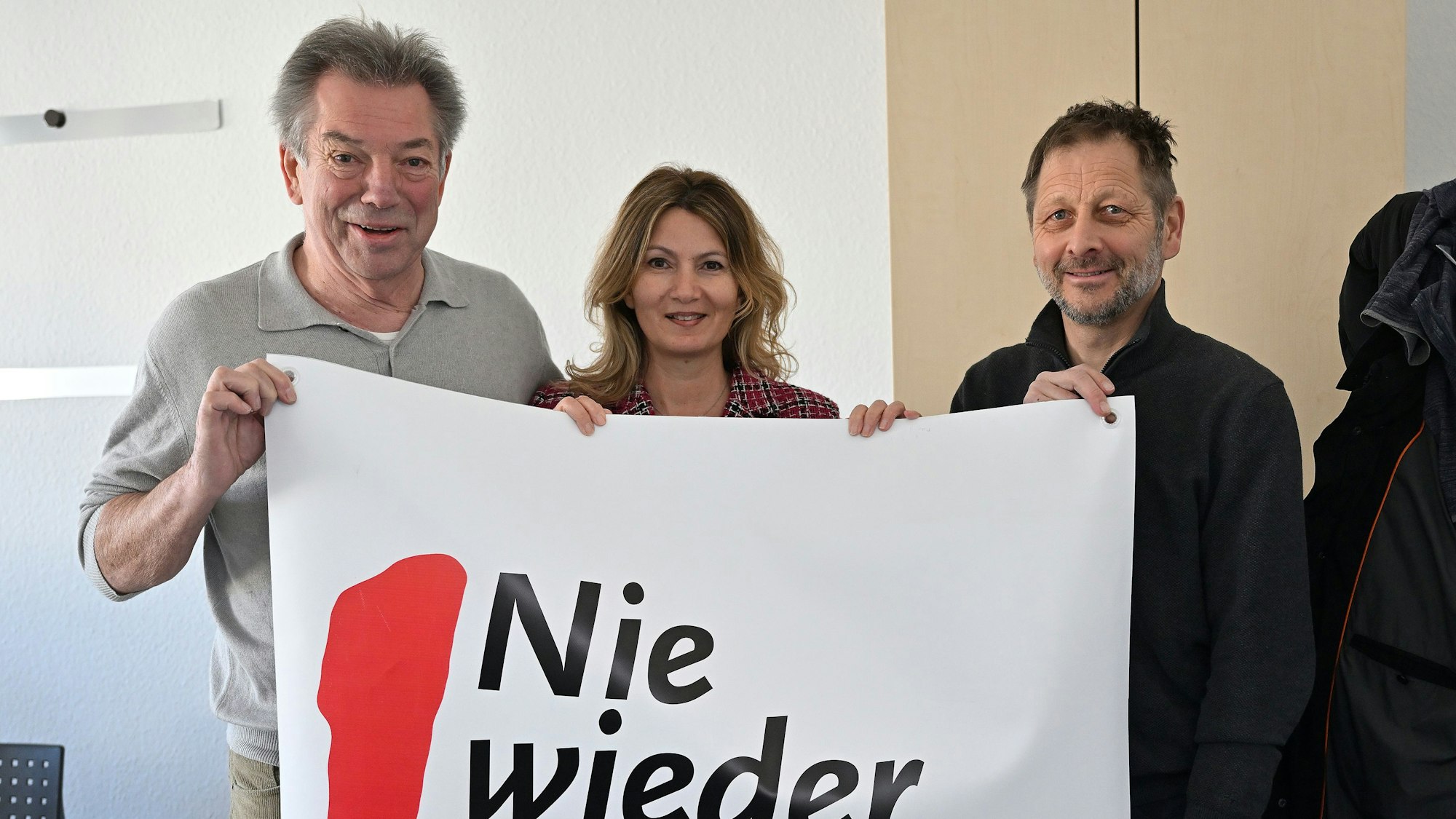 Drei Menschen halten ein Banner hoch.