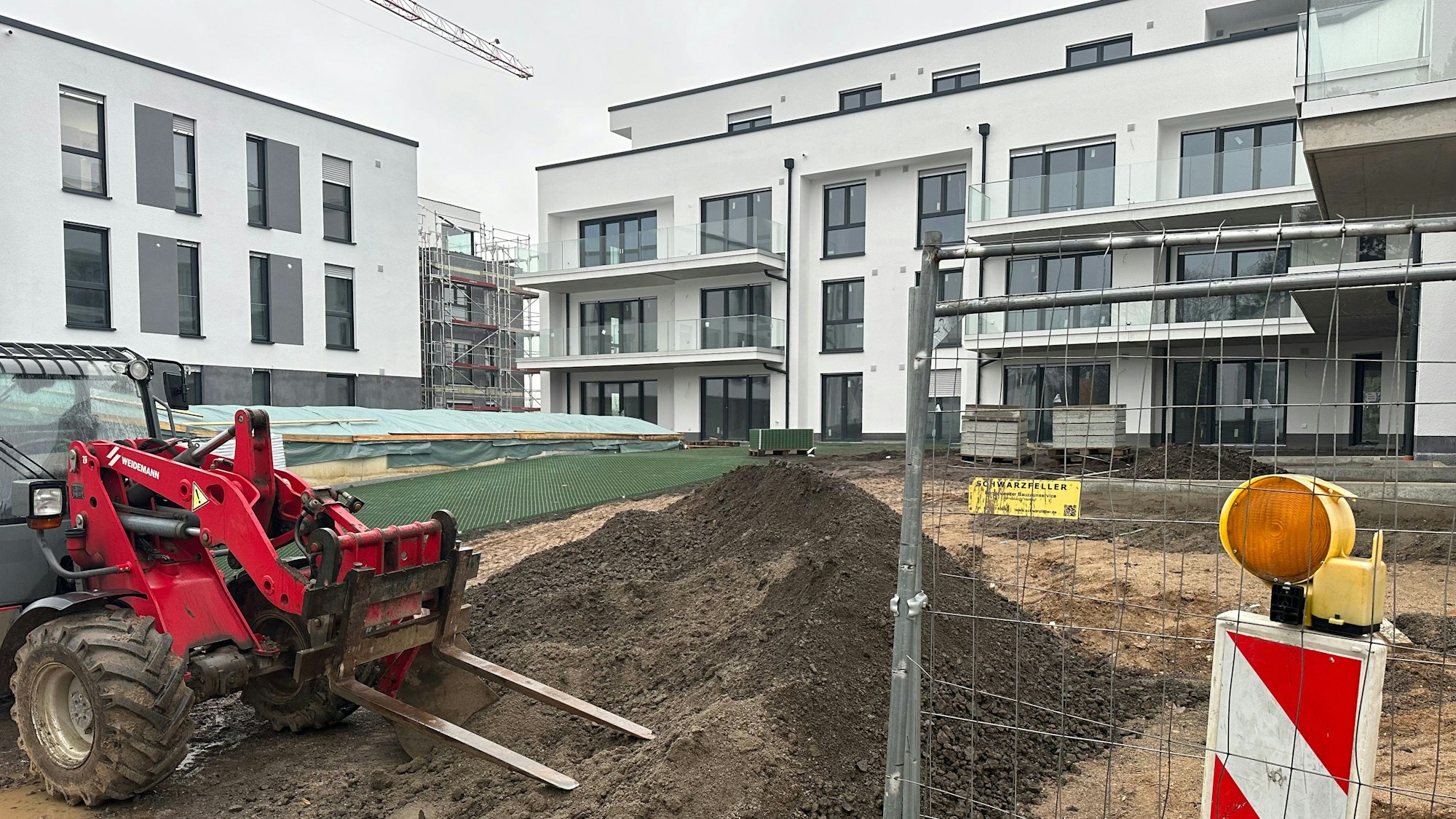 Auf dem Baugrundstück eines Mehrfamilienhaus-Projekts steht eine Baumaschine.