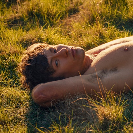 Barry Keoghan streckt sich in einer Szene von „Saltburn“ mit freiem Oberkörper im Gras aus.
