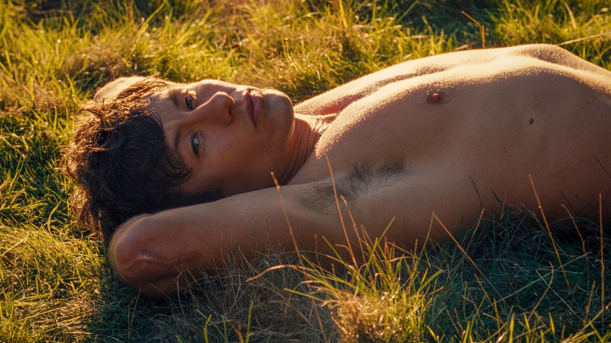 Barry Keoghan streckt sich in einer Szene von „Saltburn“ mit freiem Oberkörper im Gras aus.