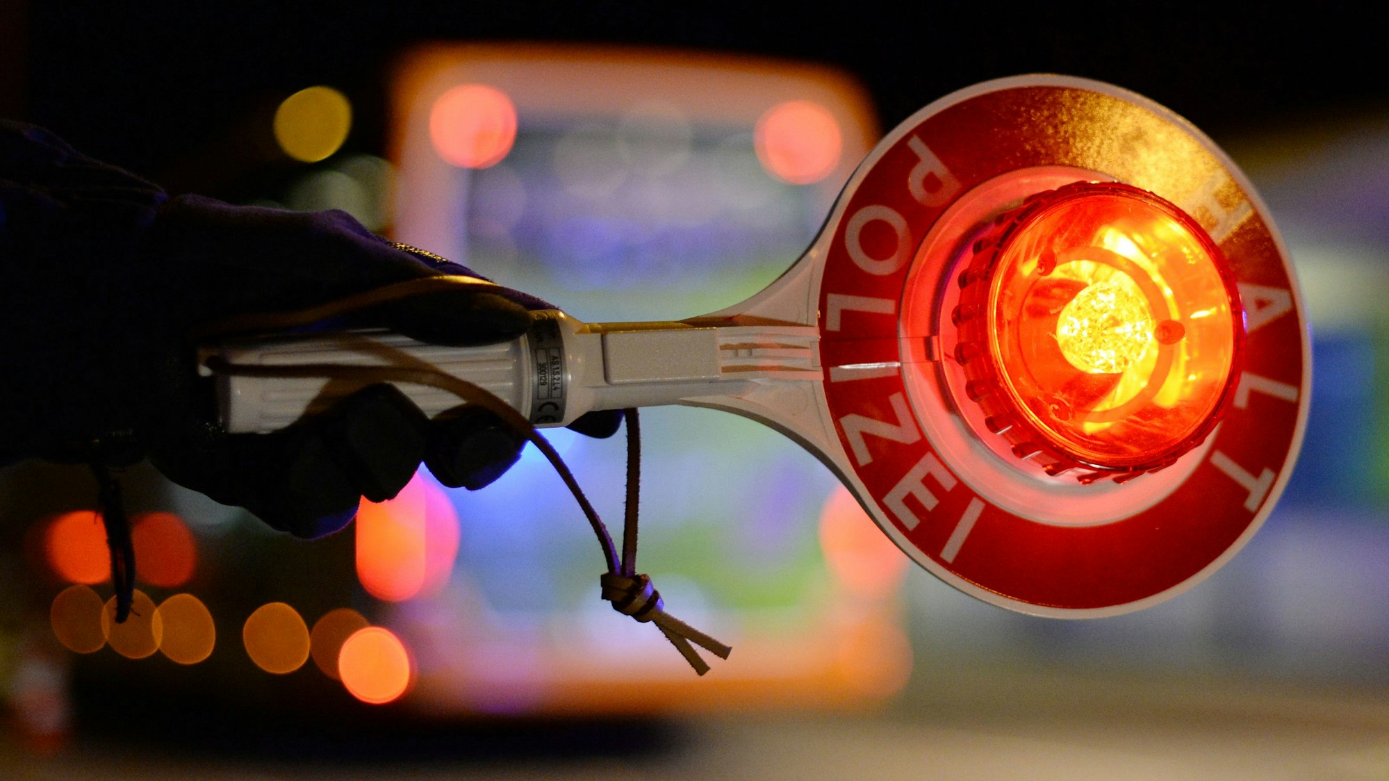 Eine behandschuhte Hand hält an einer Straße eine Kelle hoch mit der Aufforderung „Halt Polizei“.