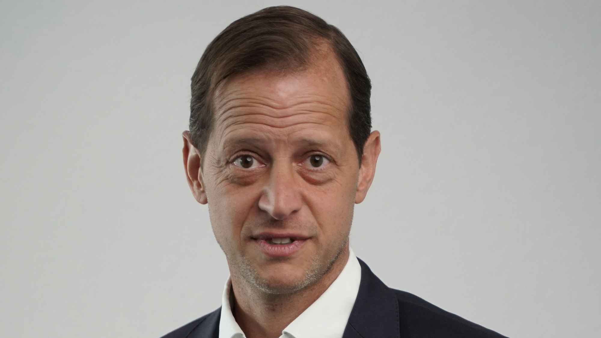 Ein Mann im Anzug steht vor einem grauen Hintergrund.