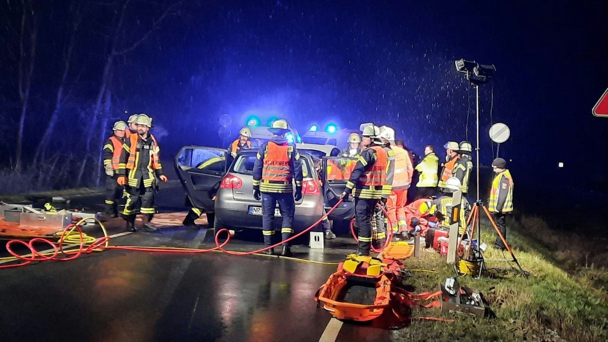 Feuerwehrleute stehen zwei Fahrzeugen, die zusammengestoßen. Rettungsmittel liegen auf der Straße bereit.