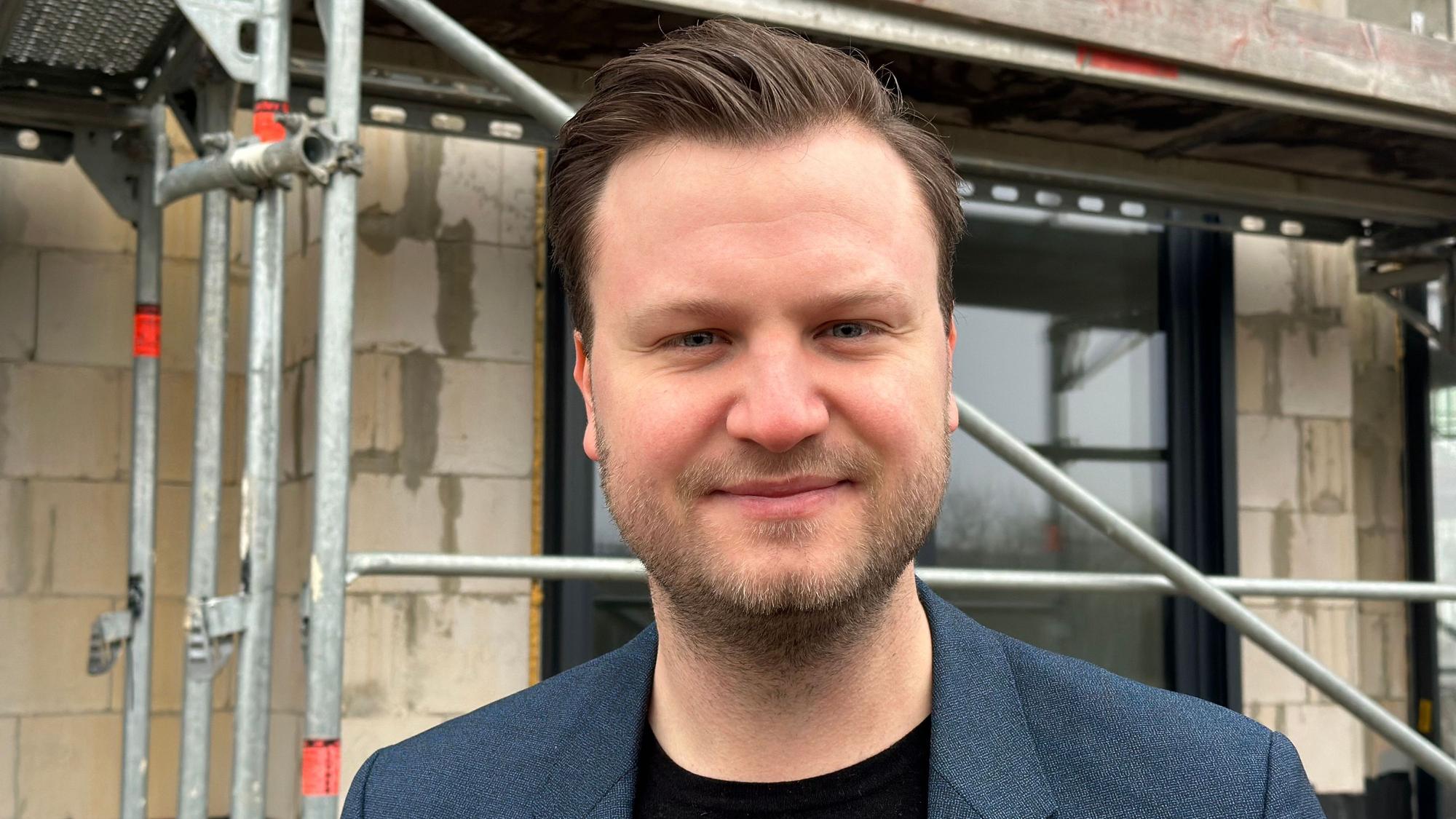 Jannis Klutinius mit Dreitagebart steht vor einem Neubau.