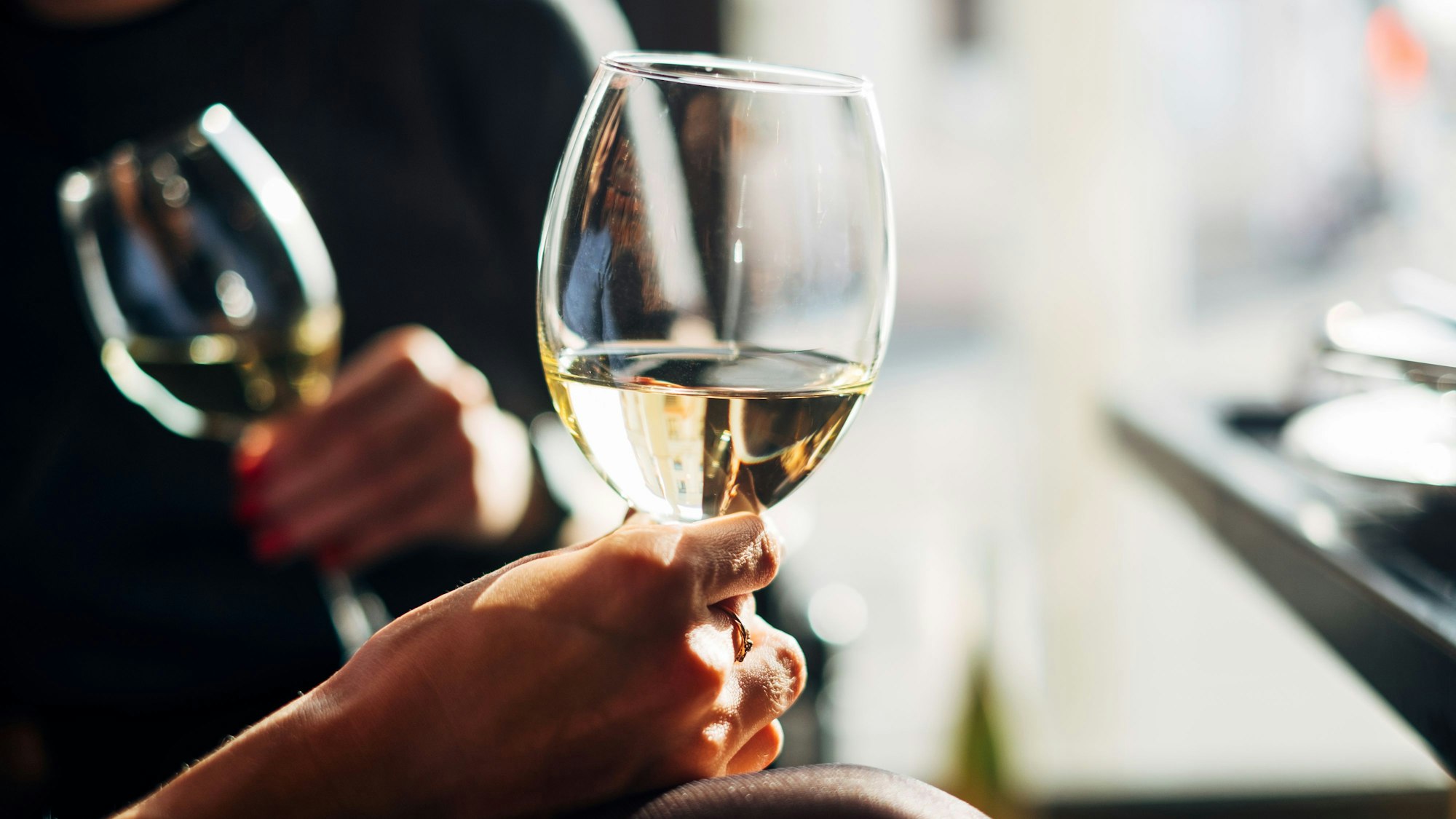 zwei Frauenhände halten Weißweingläser