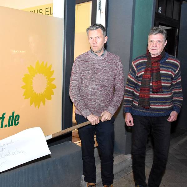 Auf dem Foto sind die Elsdorfer Grünen-Politiker Michael Broich und Hartmut Bergheim vor dem Büro ihrer Fraktion zu sehen. Broich hält die Harke in den Händen.