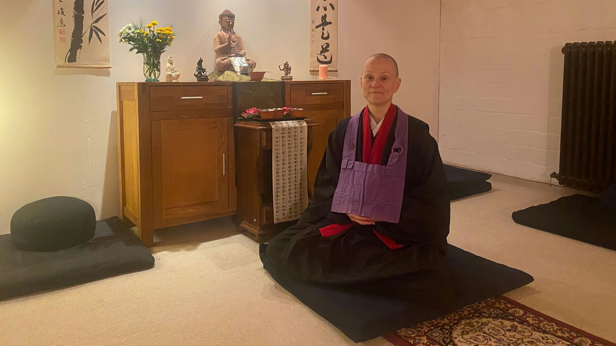 Marion GenRai kniet in einem Gewand auf einem Kissen.