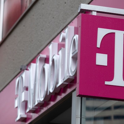 Ein Logo der Deutschen Telekom bzw. T-Mobile ist vor einem Geschäft in einer Innenstadt zu sehen.