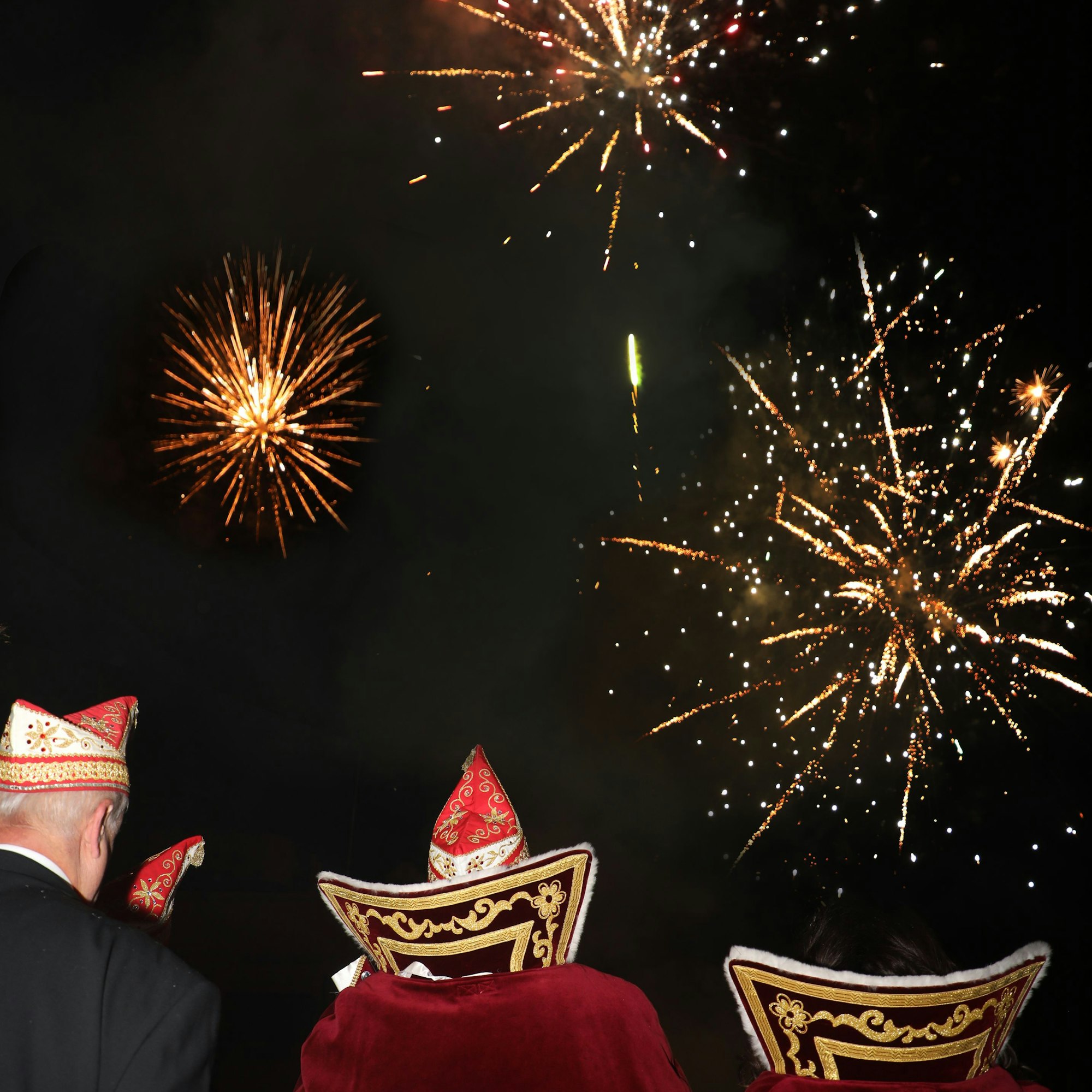 Das angehende Dreigestirn schaut zum Himmel, wo ein Feuerwerk zu sehen ist.