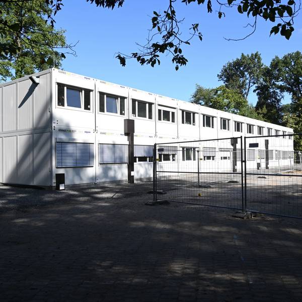 Ein großer Containerbau hinter Bauzäunen.