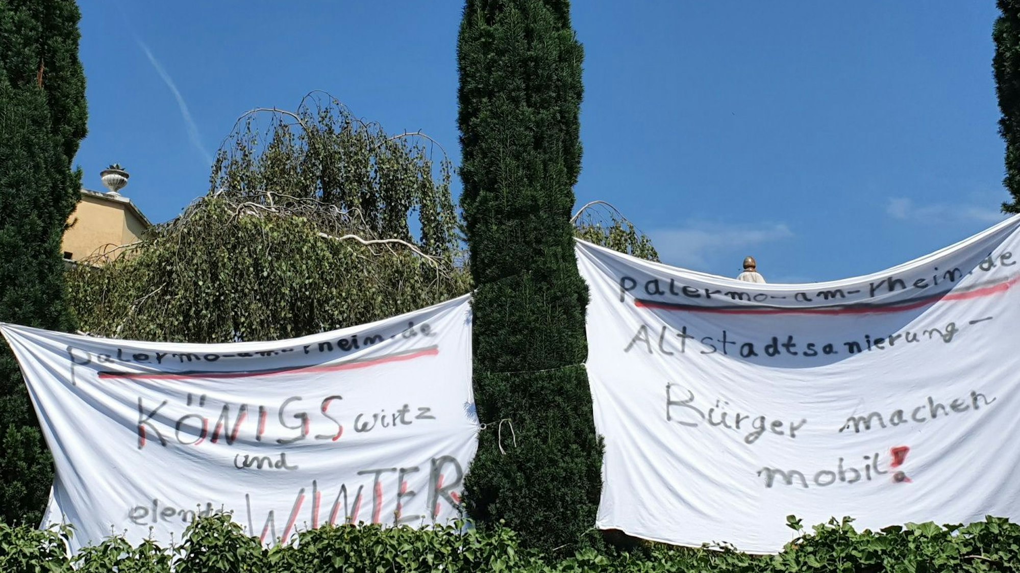 Zwischen Bäumen sind weiße Tücher gespannt, auf denen unter anderem „Bürger machen mobil“ geschrieben steht.