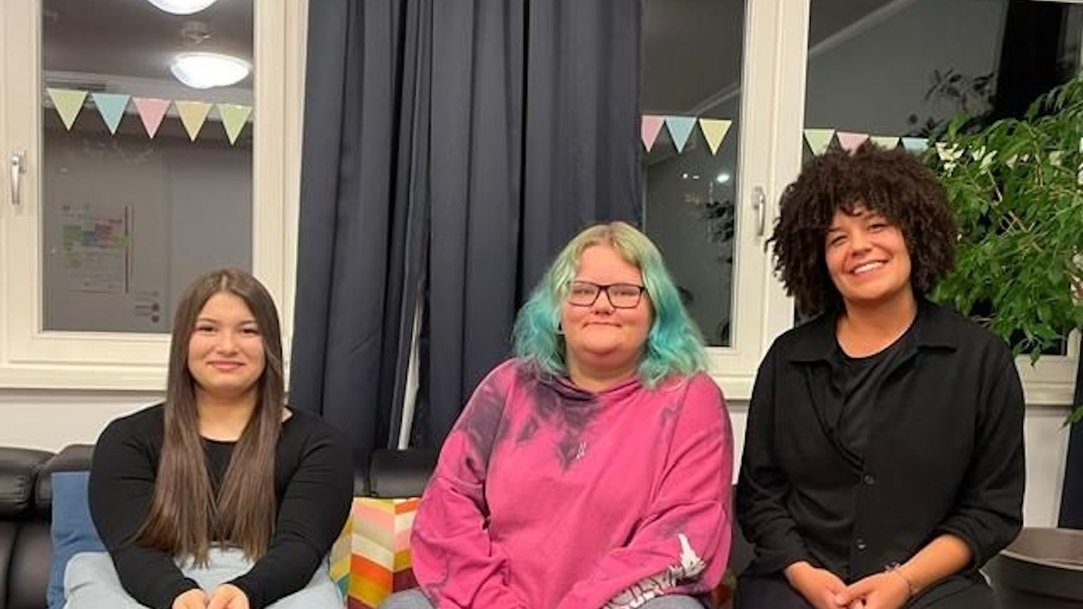 Die Bewohnerinnen der „WG Kompass“ der Diakonie Michaleshoven Dajana und Toni sitzen mit ihrer Erzieherin Alisha Anderson auf einem Sofa