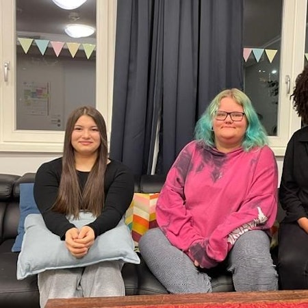 Die Bewohnerinnen der „WG Kompass“ der Diakonie Michaleshoven Dajana und Toni sitzen mit ihrer Erzieherin Alisha Anderson auf einem Sofa