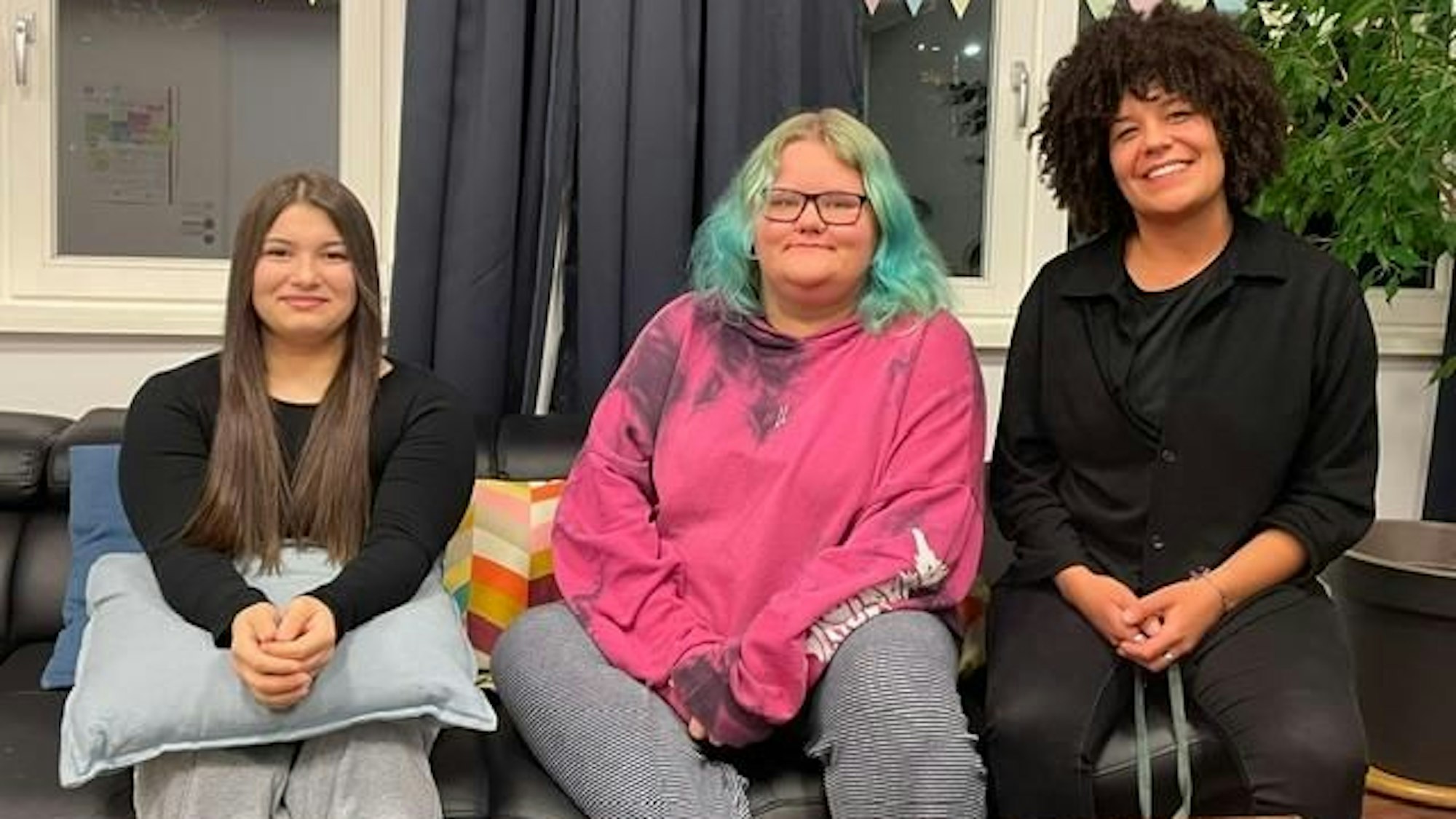 Die Bewohnerinnen der „WG Kompass“ der Diakonie Michaleshoven Dajana und Toni sitzen mit ihrer Erzieherin Alisha Anderson auf einem Sofa