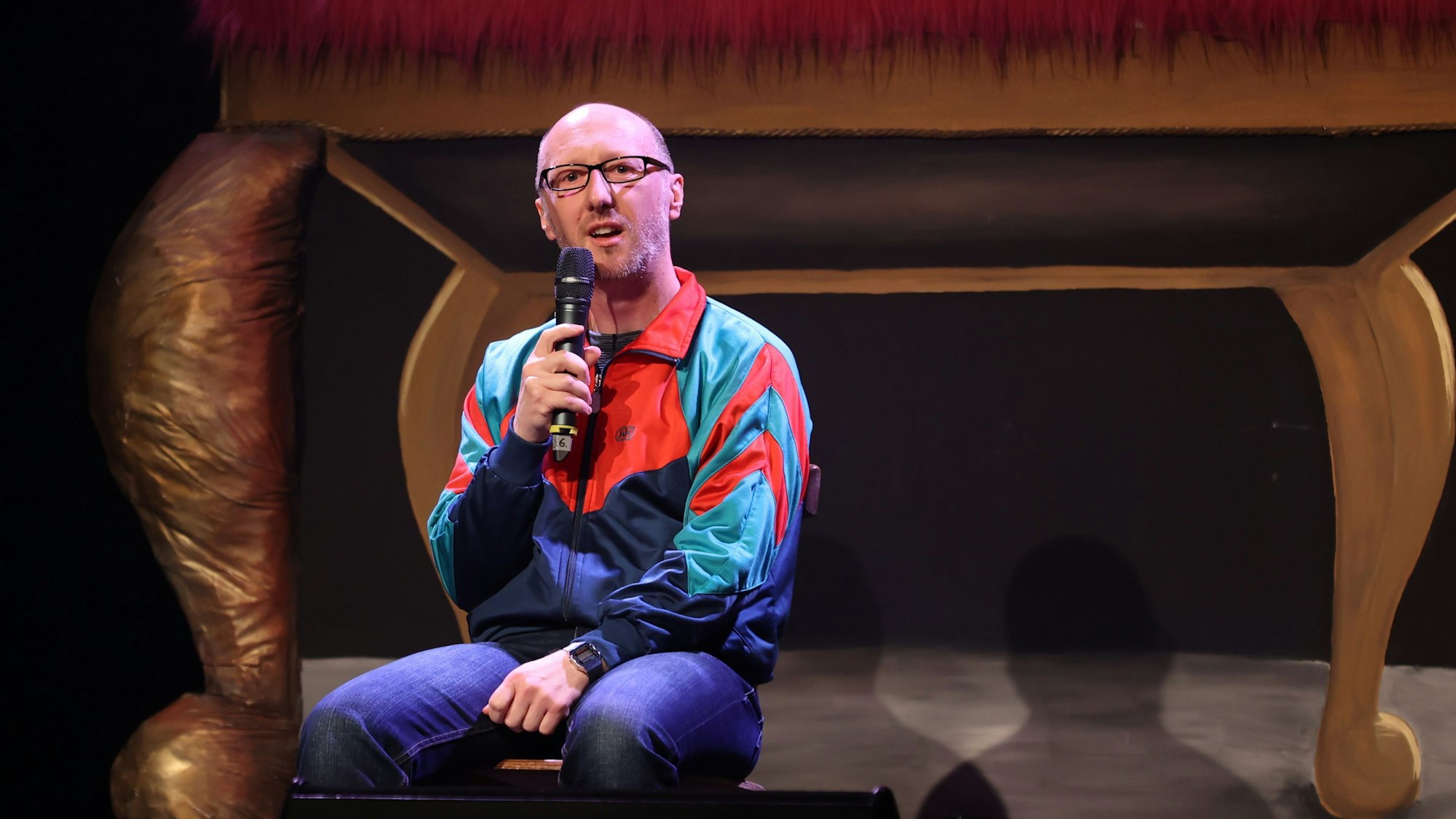 Ralf Senkel sitzt auf der Bühne und spricht ins Mikrophon