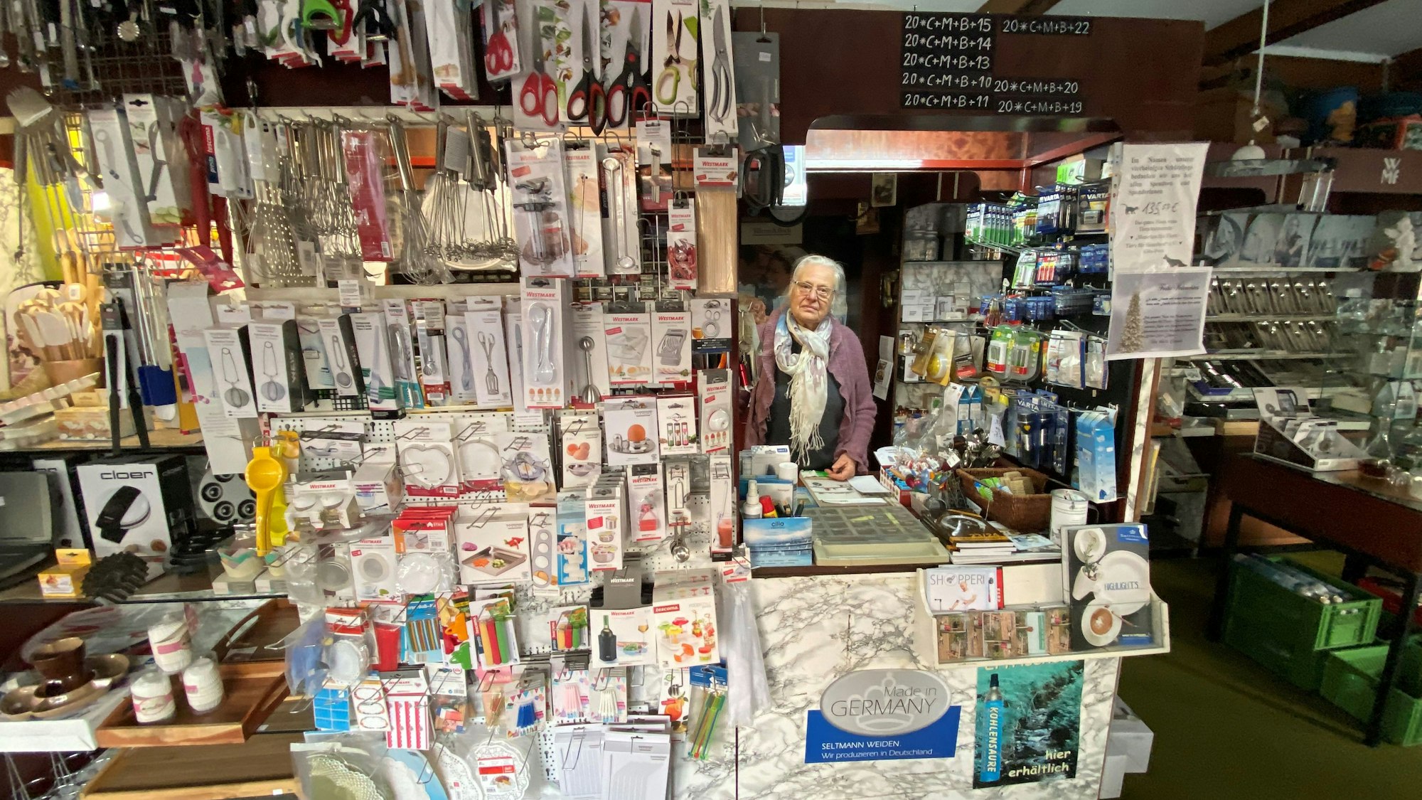 Hinter der Ladentheke steht eine alte Dame.
