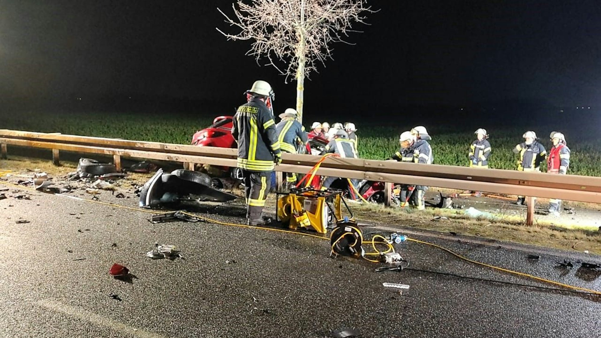 Feuerwehrleute arbeiten an nach einem schweren Verkehrsunfall an einem Auto, das hinter einer Leitplanke neben der Straße liegt.