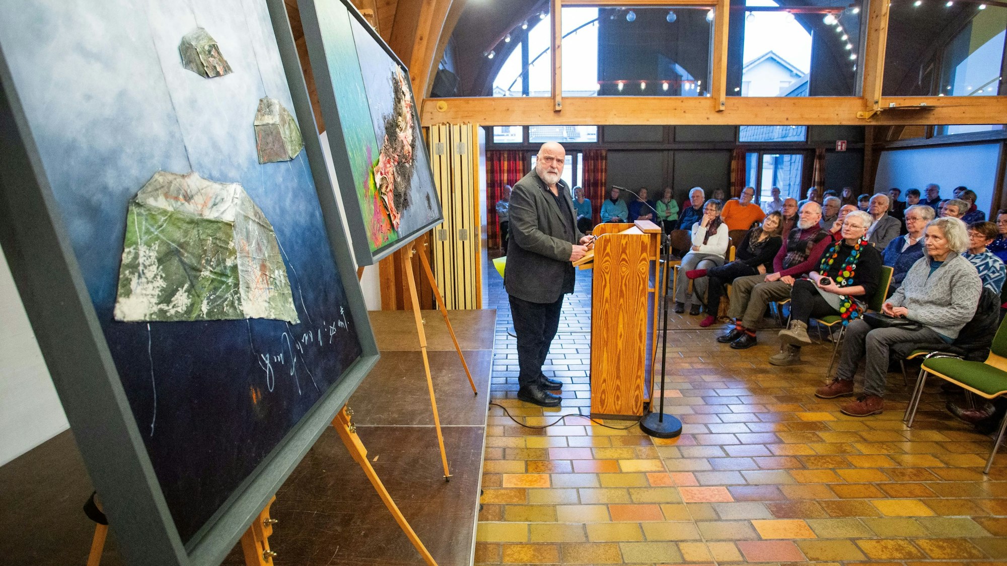 Künstler Uwe Appold hält einen Vortrag. Hinter ihm stehen mehreren Bilder.