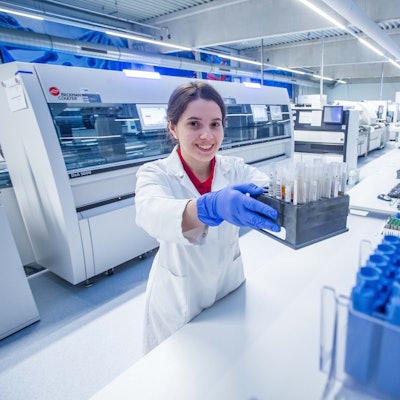 Eine Frau mit Kittel hält in einem Labor eine Kiste mit Probenröhrechen in der Hand.