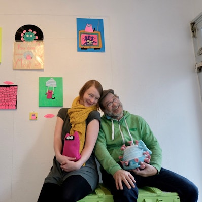 Ein Mann und eine Frau sitzen aneinandergelehnt nebeneinander und lachen in die Kamera.