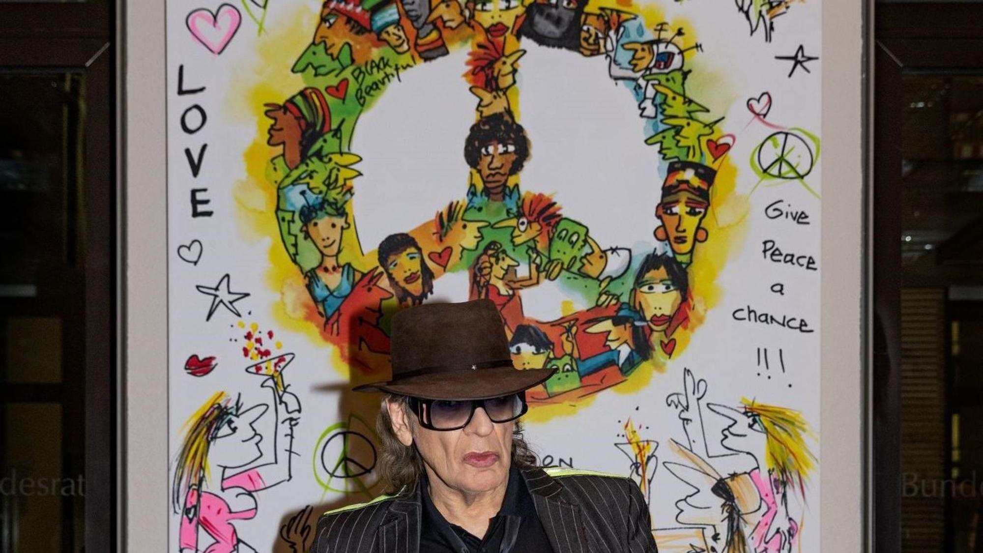 HANDOUT - 23.02.2023, Berlin: Der Musiker Udo Lindenberg steht im Bundesrat vor seinem Gemälde «Wir ziehen in den Frieden». Der Panikrocker will für viel Geld das großformatige Kunstwerk versteigern. Der Gewinn soll dem Hamburger Verein Arche zugute kommen, der Kindern und Jugendlichen hilft.
