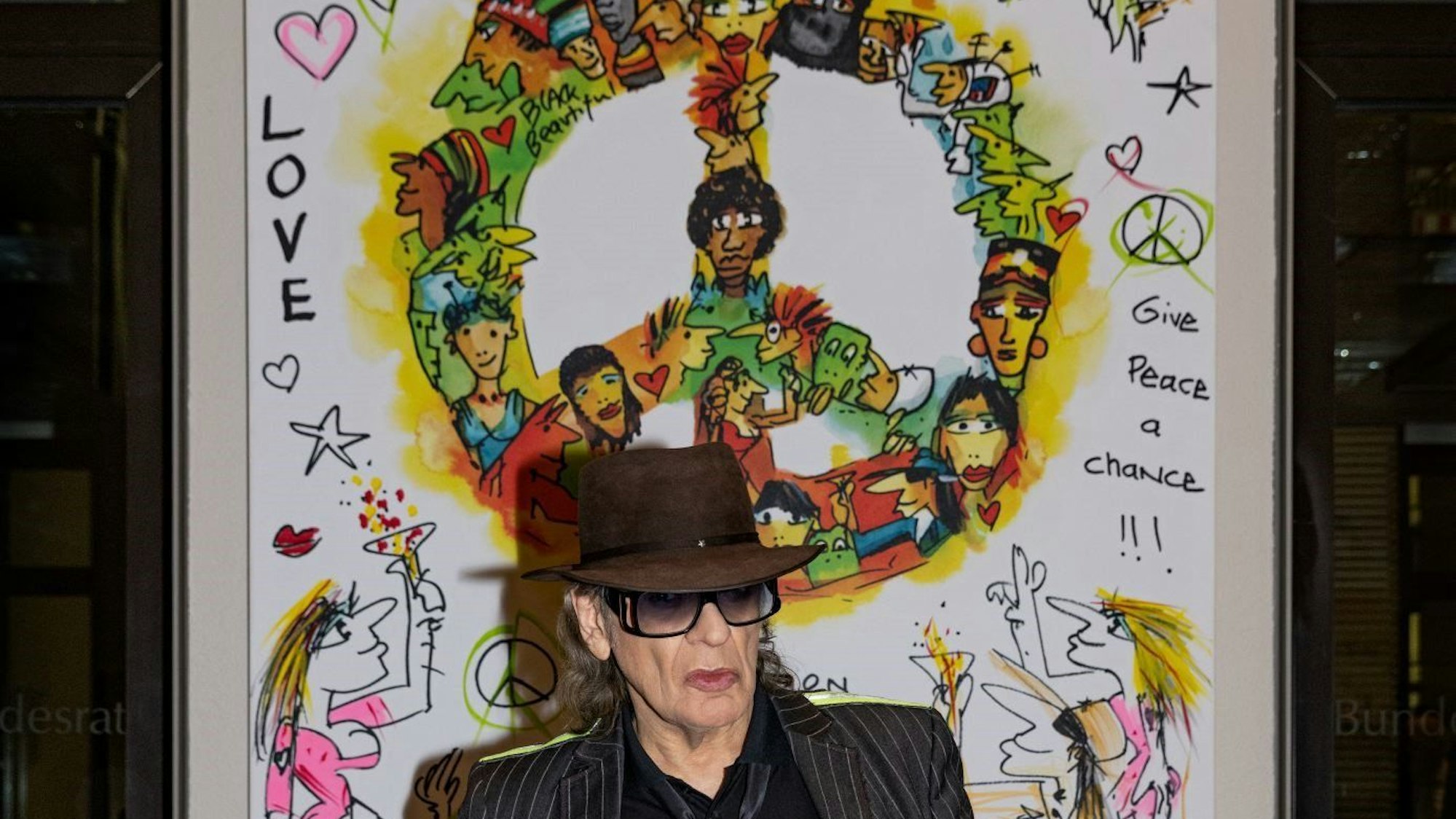 HANDOUT - 23.02.2023, Berlin: Der Musiker Udo Lindenberg steht im Bundesrat vor seinem Gemälde «Wir ziehen in den Frieden». Der Panikrocker will für viel Geld das großformatige Kunstwerk versteigern. Der Gewinn soll dem Hamburger Verein Arche zugute kommen, der Kindern und Jugendlichen hilft.