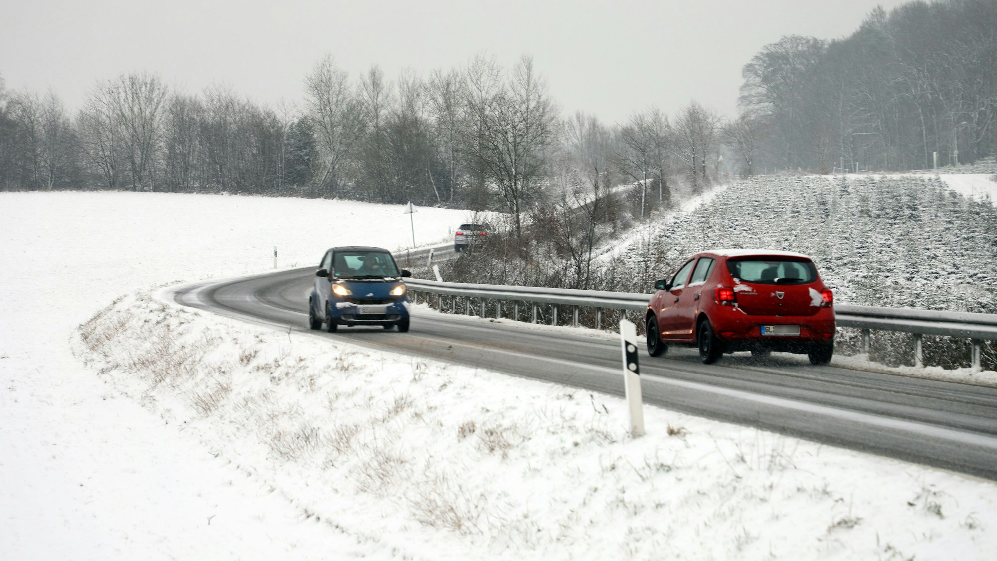 Zwei Autos fahren auf einer winterlichen Straße durch eine schneebedeckte Landschaft.