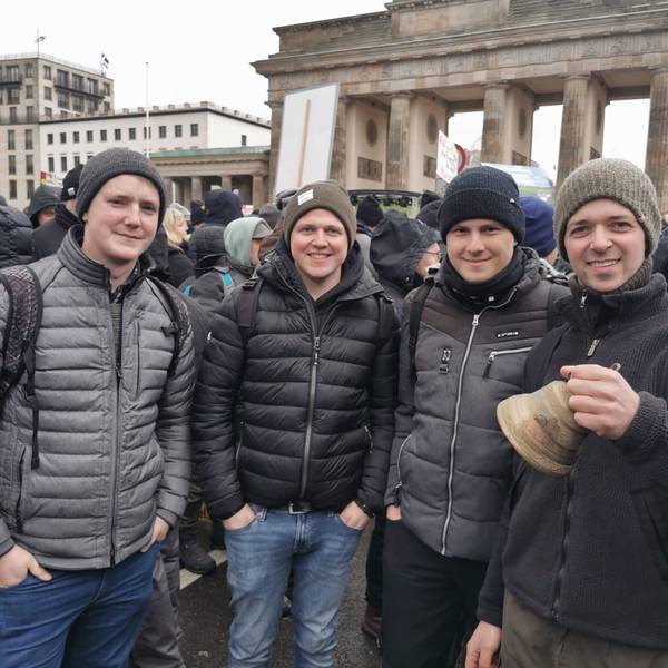 Vier junge Männer stehen vor dem Brandenburger Tor in Berlin.