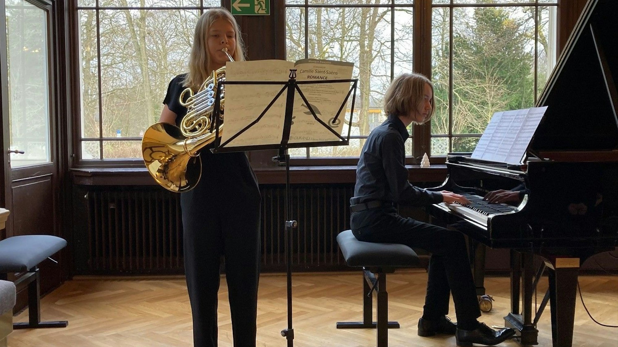 Ein Junge sitzt an einem Flügel, ein Mädchen spielt Hotn.