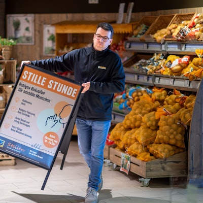 Dirk Steilen trägt in seinem Edeka-Markt einen Aufsteller, der auf die Stille Stunde hinweist, in der auf grelles Licht und Werbung verzichtet wird.