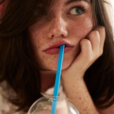 gelangweiltes Mädchen liegt mit Strohhalm im Mund auf dem Bett