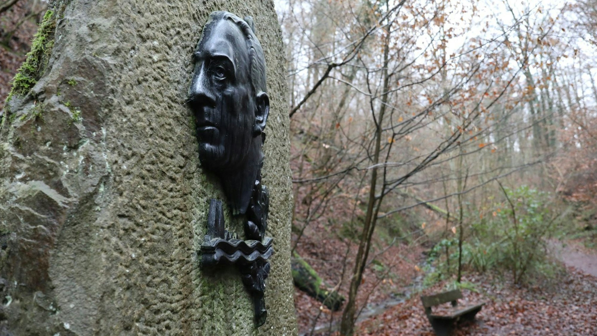 An einem großen Stein ist Bronzerelief mit einem Porträt von Willi Ostermann angebracht.