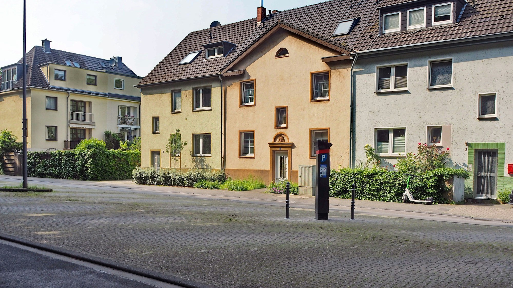 Vor Reihenhäusern ist eine große Parkfläche mit einem Parkscheinautomaten zu sehen.