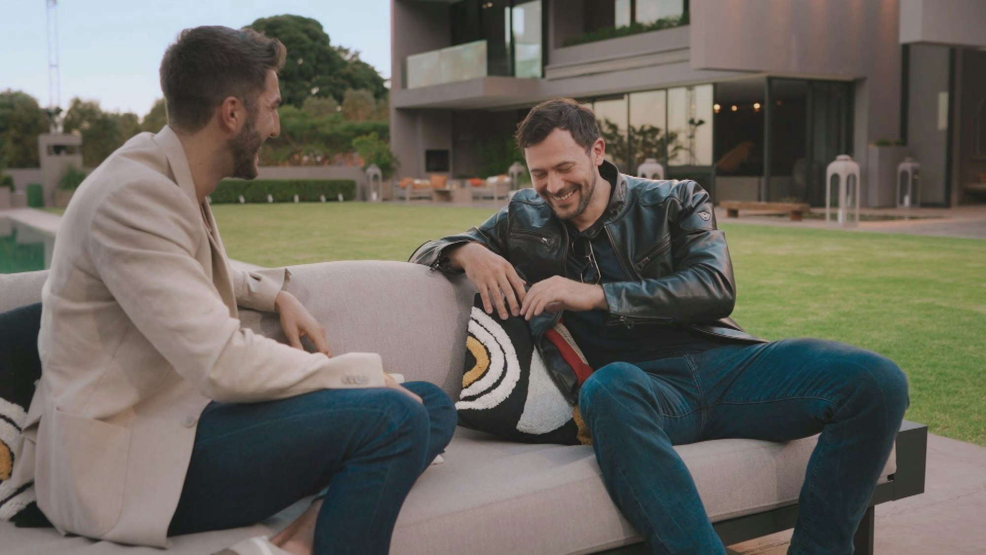 Zwei Männer sitzen lachend auf einer Couch.