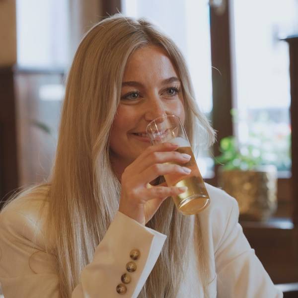 Eine Frau mit blonden Haaren hat ein Kölsch in der Hand und lacht ihr Gegenüber an.